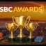 Golden trophies on a roulette table with dice and poker chip, Lisbon skyline and SBC Awards logo in the background