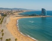 A panoramic view of Barcelona’s beachfront showing the W Hotel, golden sands, and the Mediterranean Sea under clear blue skies.