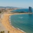 A panoramic view of Barcelona’s beachfront showing the W Hotel, golden sands, and the Mediterranean Sea under clear blue skies.