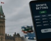 Hand holding smartphone displaying sports betting app with Parliament Hill Peace Tower in background, representing Canada's Bill S-211 advertising regulations