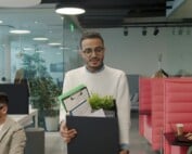 Mann verlässt mit einem Karton seinen Arbeitsplatz aufgrund von Entlassung.