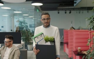 Mann verlässt mit einem Karton seinen Arbeitsplatz aufgrund von Entlassung.