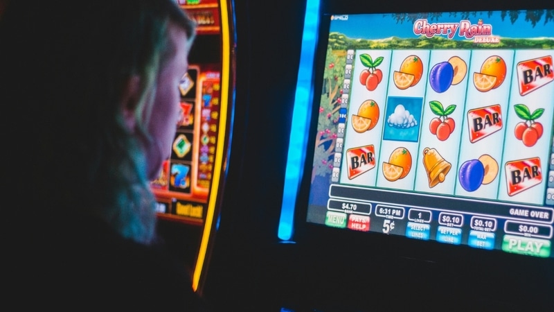 Casino-Spieler vor einem Spielautomaten mit Fruchtsymbolen.